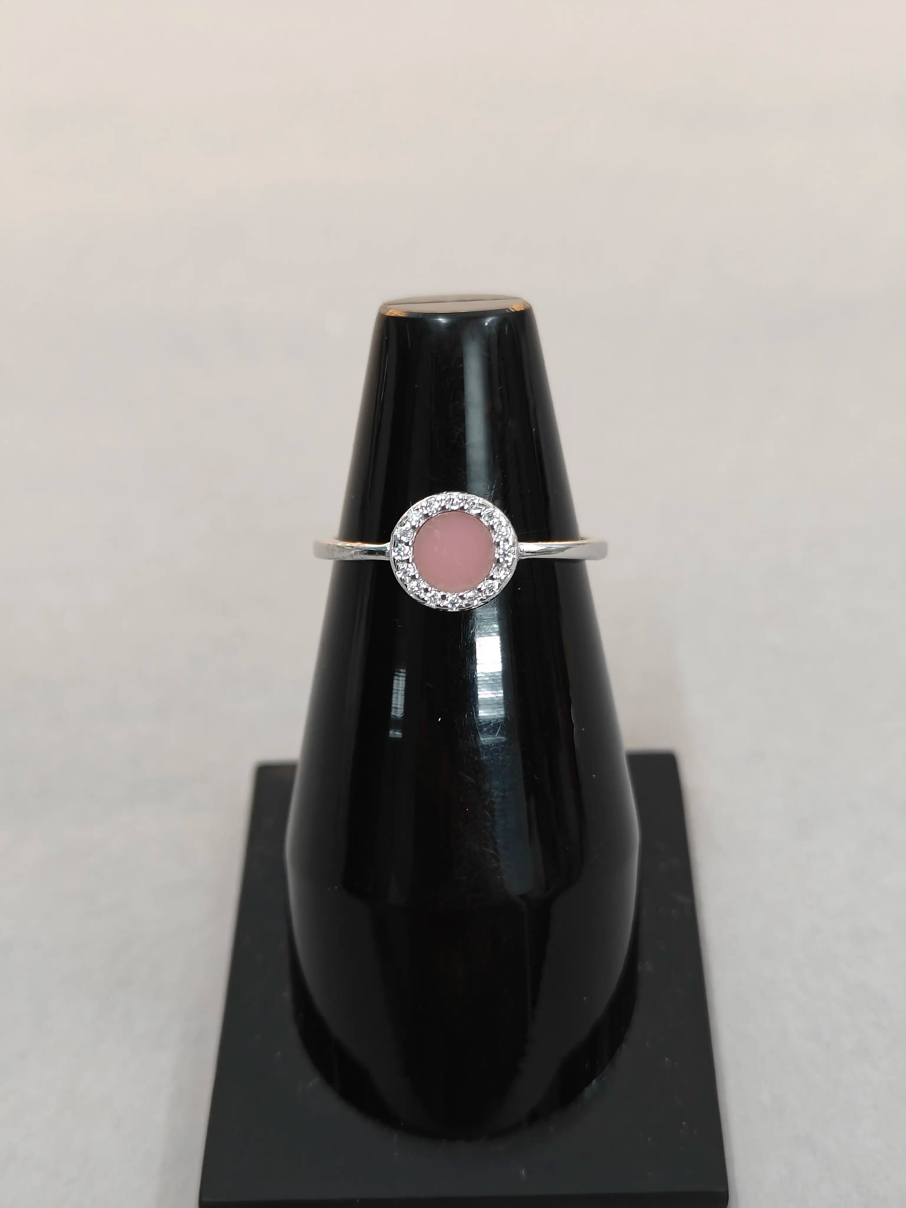 Silver ring with a pink stone on a black stand against a light gray background